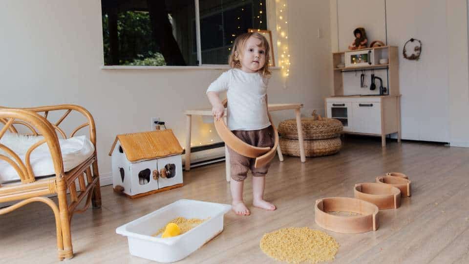 A little girl is playing with a bowl of rice in a living room. (rice, playing)