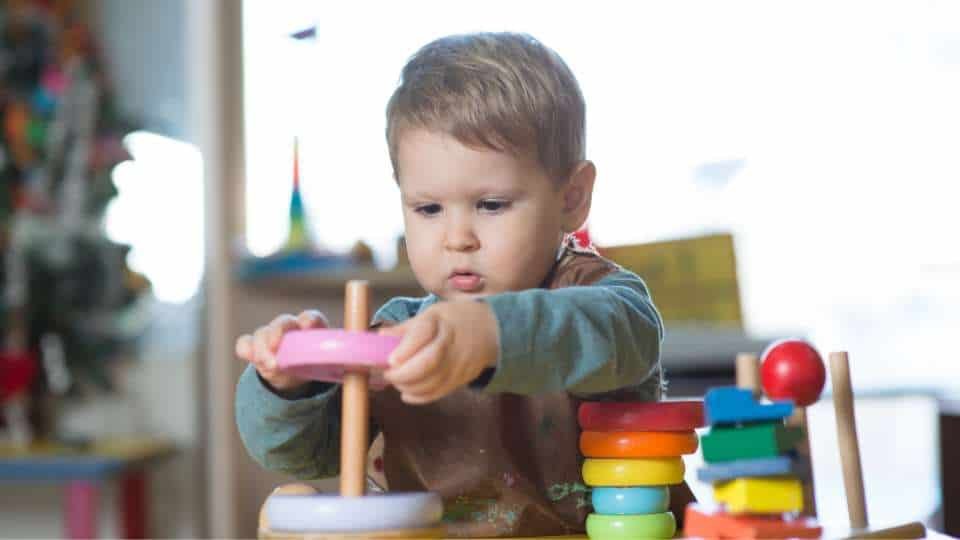 Un tout-petit travaille sa logique et sa réflexion grâce à des jouets en bois Montessori posés à une table.